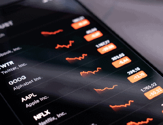 Close-up of a smartphone displaying a stock market app with orange line charts and ticker prices for GOOG, AAPL, and NFLX.