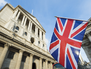 Stone neoclassical government building with a Union Jack flag flying in the foreground against a blue sky.