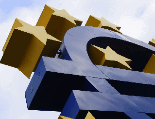 Close-up of a large blue euro symbol sculpture with yellow block shapes and EU stars against a cloudy sky.