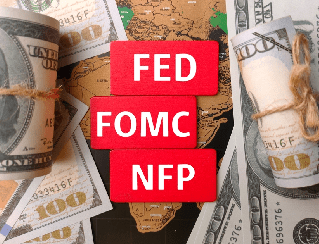 Red blocks labeled FED, FOMC, and NFP stacked in front of rolled dollar bills, symbolizing U.S. monetary policy and economic data.