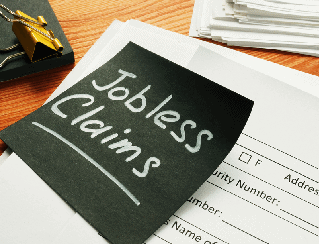 Chalkboard reading 'Jobless Claims' on a desk next to stacked papers and a gold binder clip.