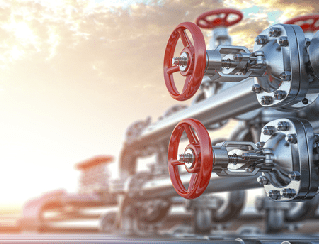 Industrial valves with red circular handwheels in the foreground along a metal pipeline system at an industrial site.