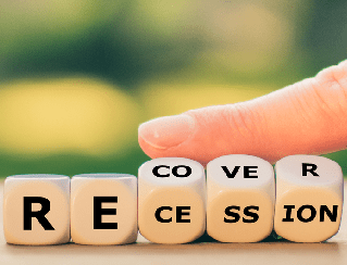 Wooden letter cubes arranged to spell 'RECESSION' with a blurred green background.