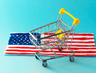 Mini shopping cart on top of an American flag against a blue background, symbolizing American consumerism.