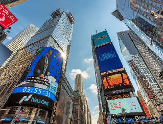 Busy city square with towering buildings and bright digital billboards displaying ads and stock data.