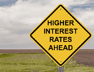 Yellow diamond warning sign reading 'Higher interest rates ahead' in a rural landscape.