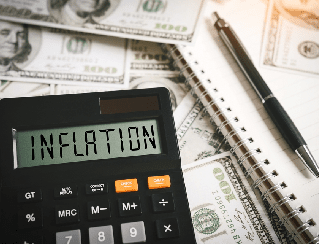 Calculator showing the word 'INFLATION' with dollar bills, a notebook, and a pen nearby.
